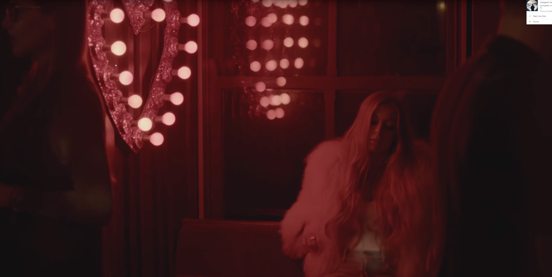 Singer in fur coat bathed in deep red light with glowing heart-shaped vanity mirror behind