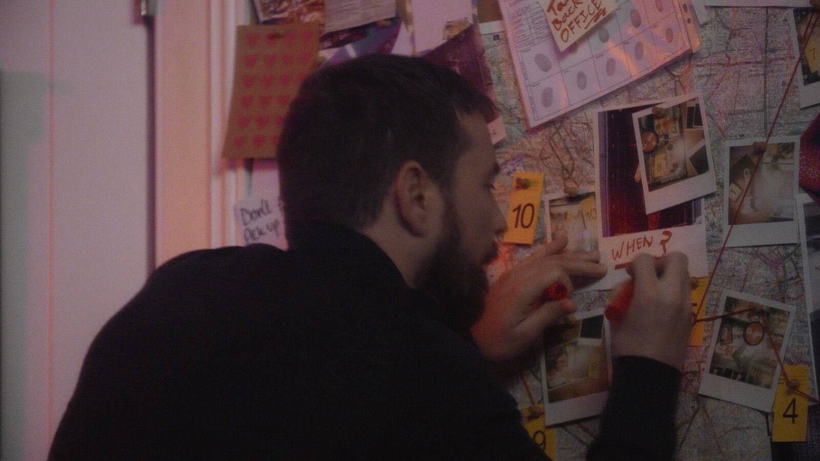 Man pinning evidence to investigation board with maps and polaroids