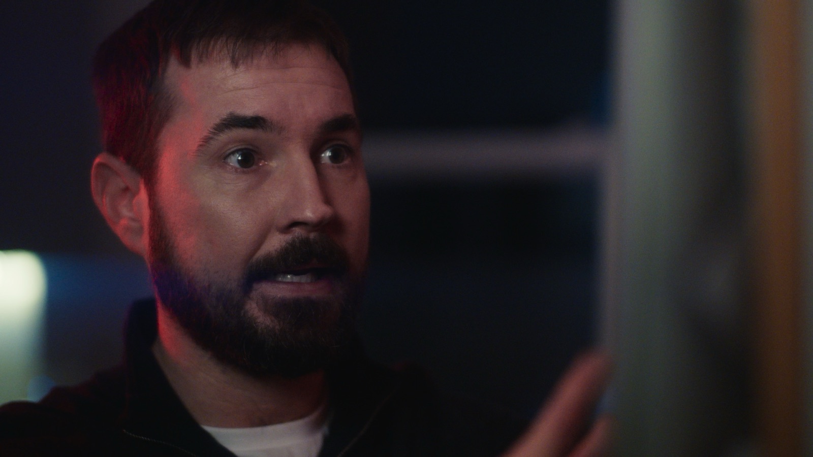 Martin Compston close-up with red and blue lighting, intense expression in dim room