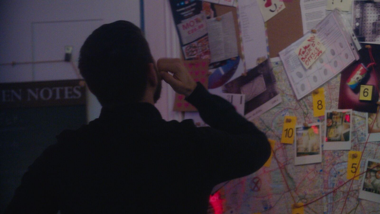 Man studying evidence board covered with maps, photos and clue markers from behind