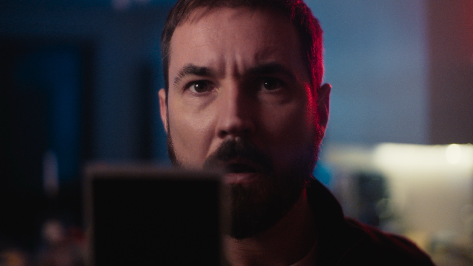 Martin Compston staring intently into camera lit by red and blue neon tones