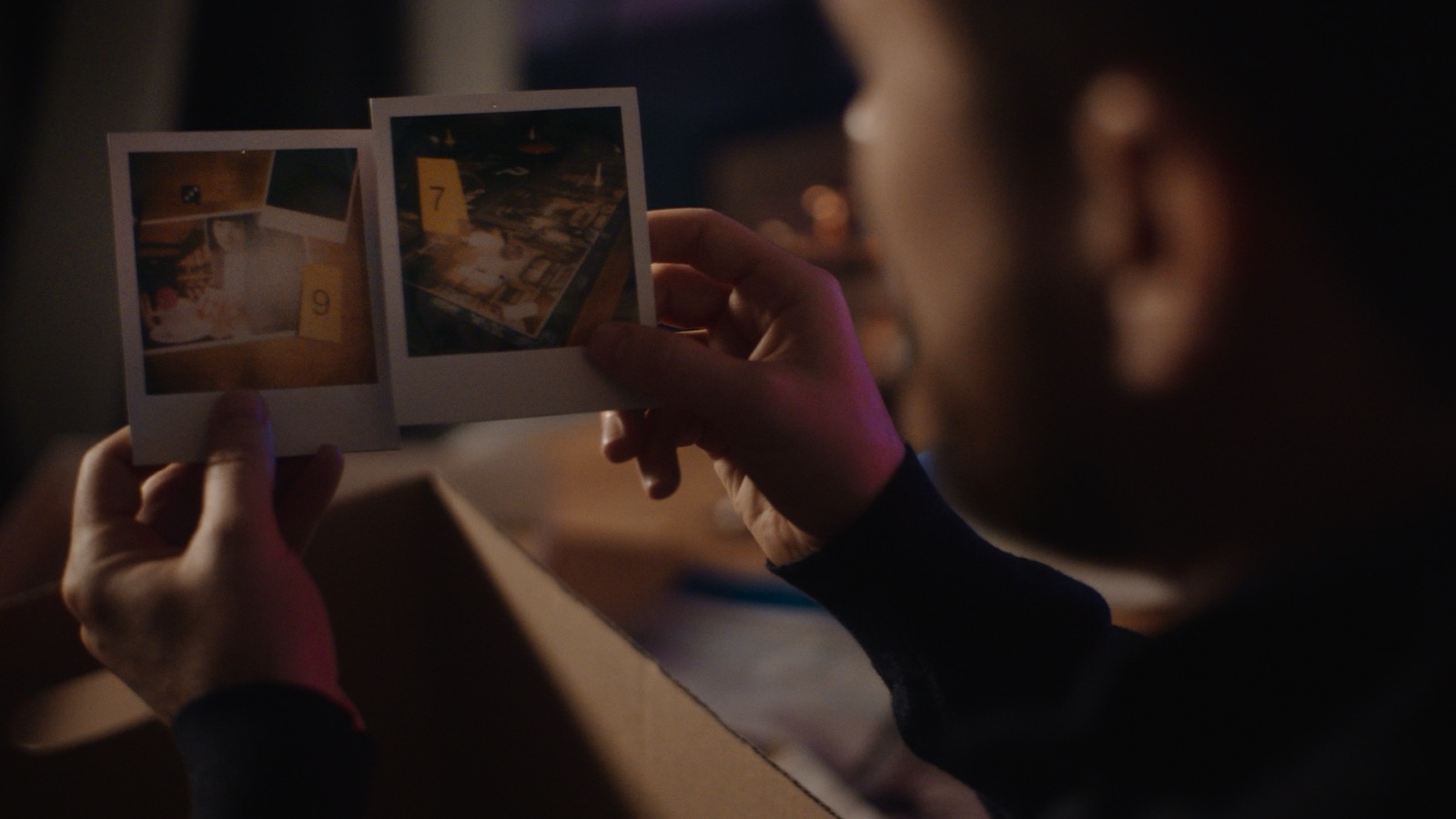 Man examining polaroid crime scene photos in a dimly lit room