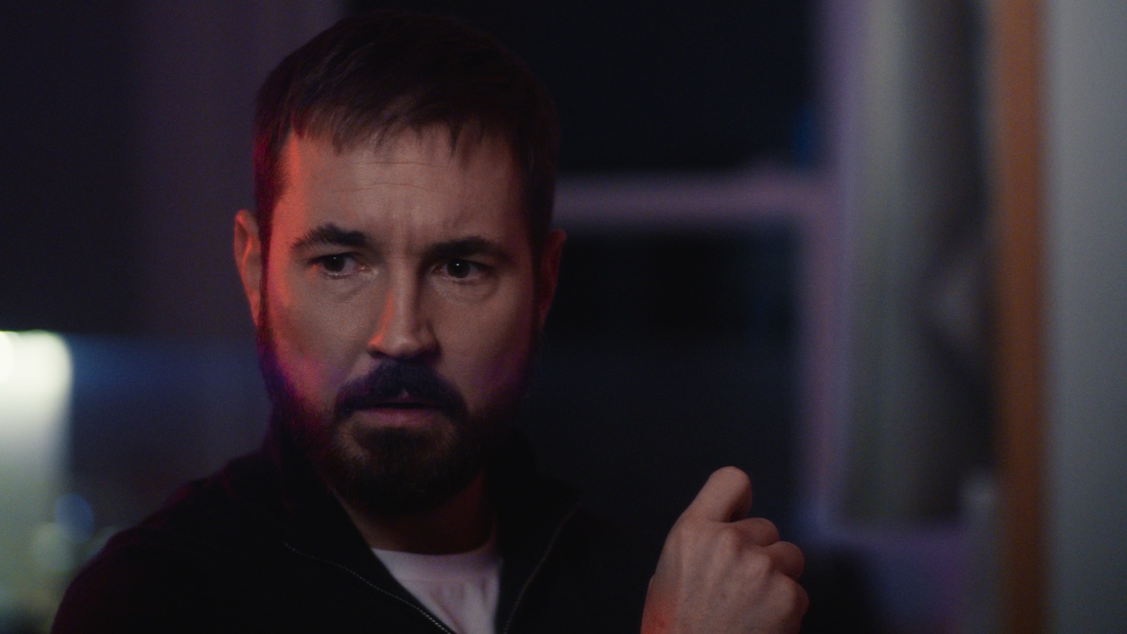Martin Compston portrait with purple-red lighting, pointing finger suspiciously