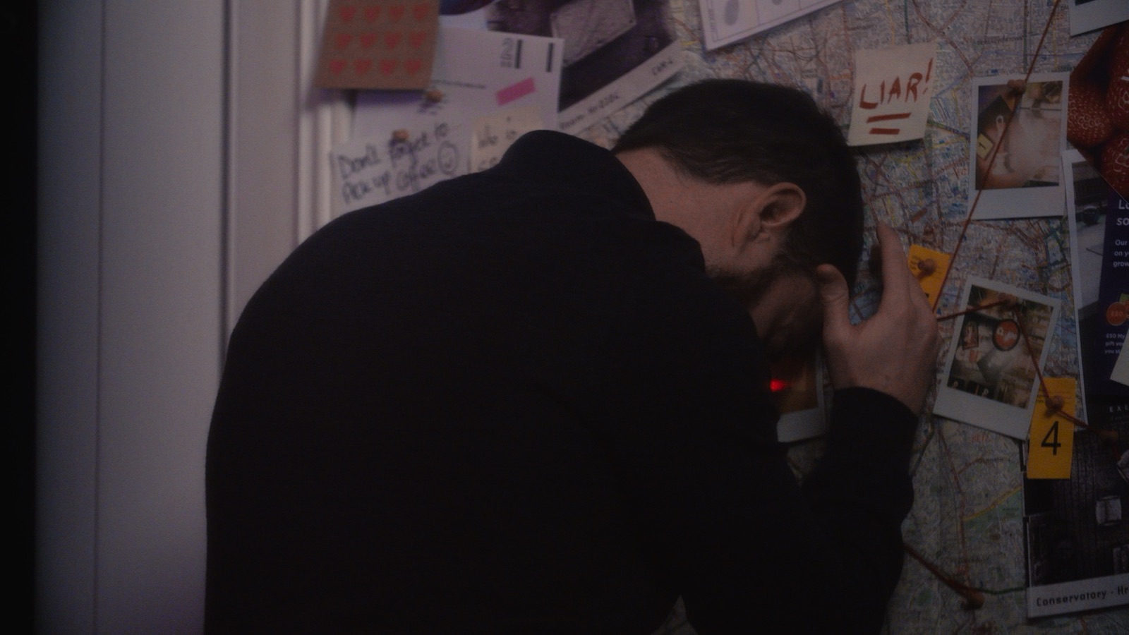 Man pressing his head against evidence board covered in clues and photos
